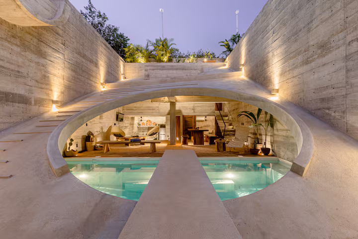 Brutalist Casa Hezbo Airbnb in Puerto Escondido with circular concrete pool opening, private swimming pool, tropical greenery, and open-air lounge area.