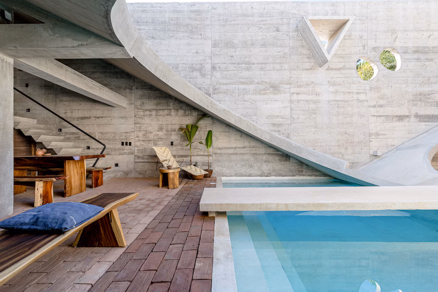 Brutalist Casa Hezbo Airbnb in Puerto Escondido with circular concrete pool opening, private swimming pool, tropical greenery, and open-air lounge area.