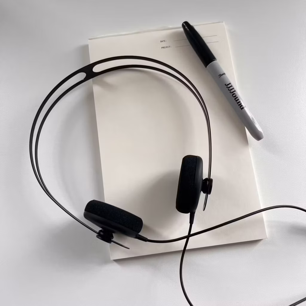 Black JJJJound x AIAIAI Tracks headphones resting on a notepad beside a black marker.