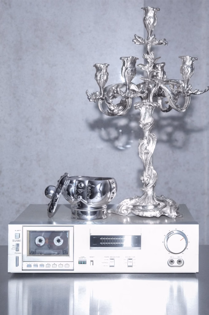 Silver Clive Christian candle and ornate candelabra displayed atop a vintage cassette deck.