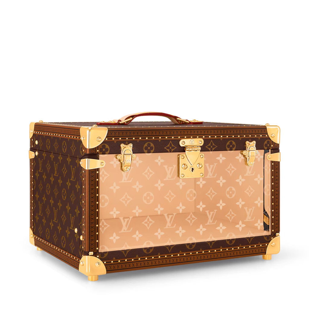 Angled view of the Louis Vuitton Shoe Box Monogram trunk showing its brown Monogram exterior, transparent front panel and gold-tone hardware.