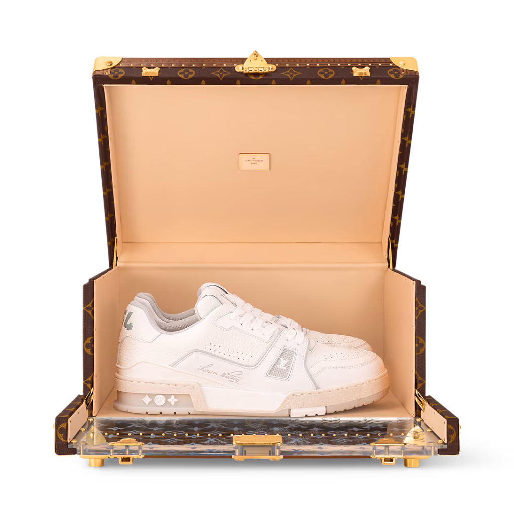 Louis Vuitton Shoe Box Monogram trunk displayed open with white sneakers, a tan interior and gold-tone hardware against a light gray background.