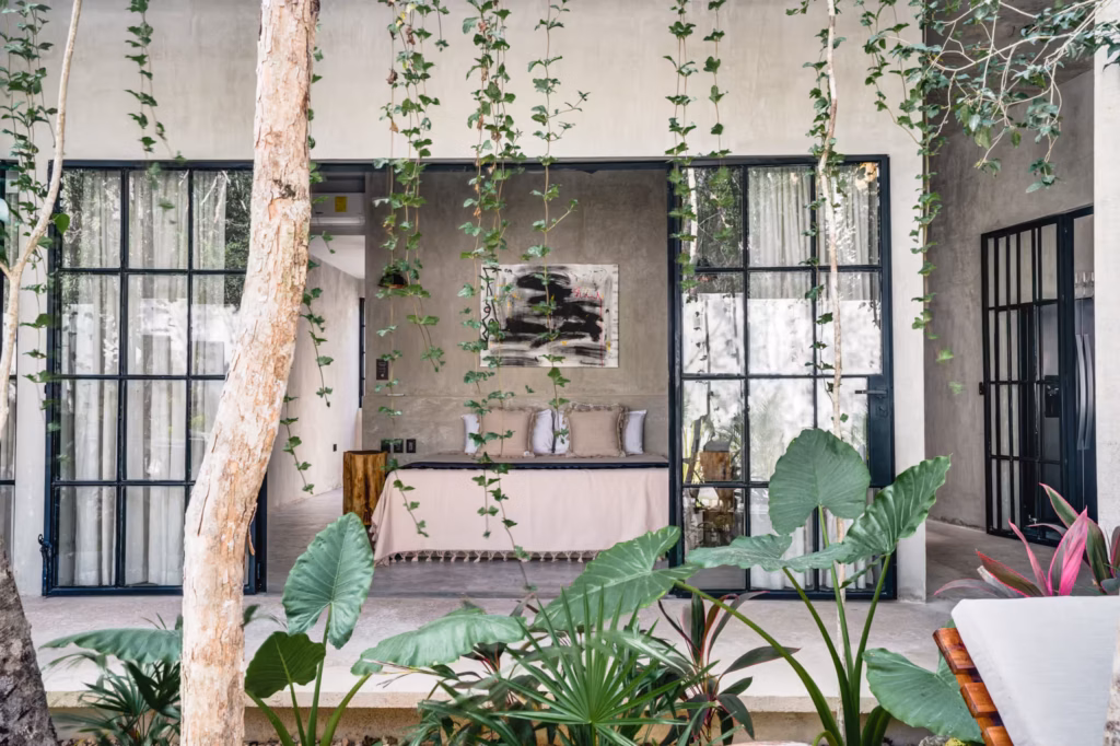 Villa Arthur 600 bedroom in Tulum featuring floor-to-ceiling glass doors, minimalist furnishings and lush tropical greenery.