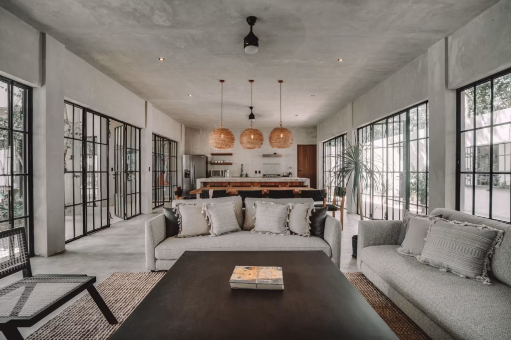 Spacious living and dining area at Villa Arthur 600 in Tulum featuring contemporary furnishings, concrete finishes and expansive windows.