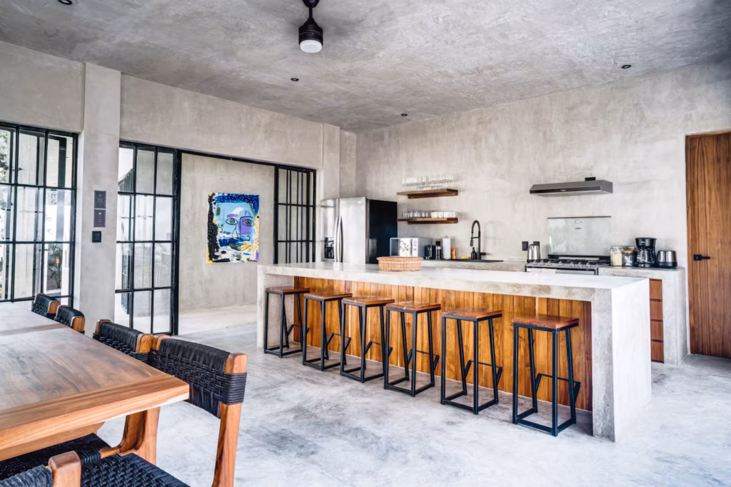 Modern kitchen at Villa Arthur 600 featuring a large breakfast bar, wooden cabinetry, woven pendant lights and an adjoining dining area.